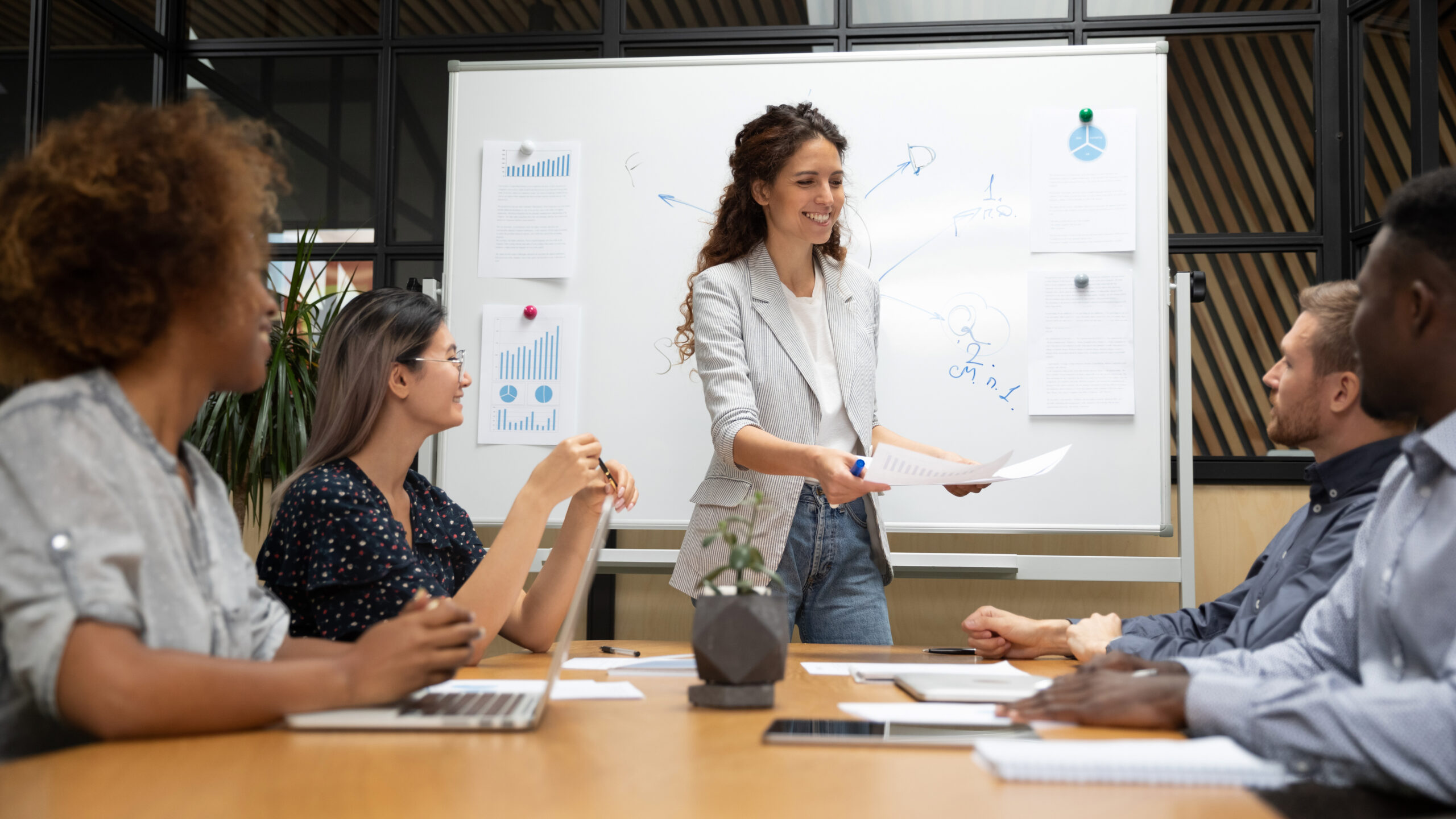 Woman presenting a diagram on a whiteboard to a group during a team meeting.