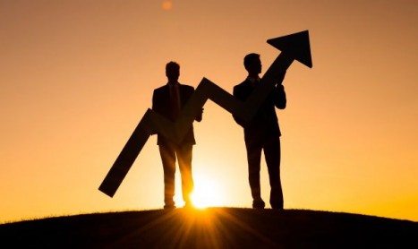 Two silhouetted businesspeople at sunset holding large upward arrows, signaling growth and success.