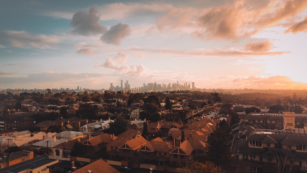 Sunset over a suburban neighborhood with a distant city skyline on the horizon and warm orange light over the scene.