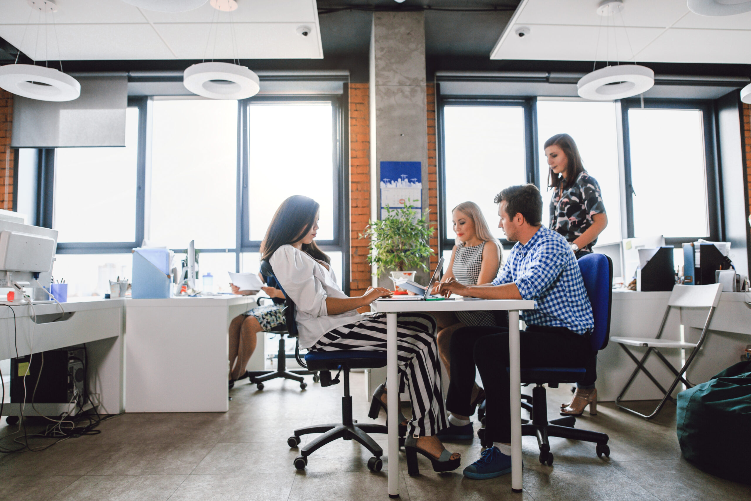 Group of colleagues working at a shared desk in a bright open-plan office.