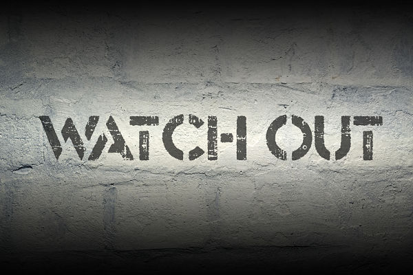 Stencil graffiti on a rough concrete wall reading 'WATCH OUT'.