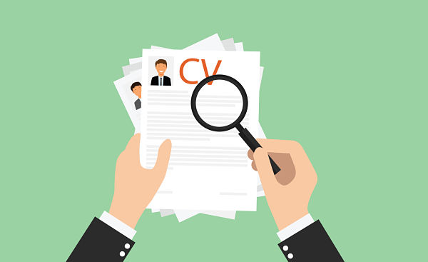 Two hands in business attire hold a stack of CVs as a magnifying glass inspects one resume, suggesting screening candidates.