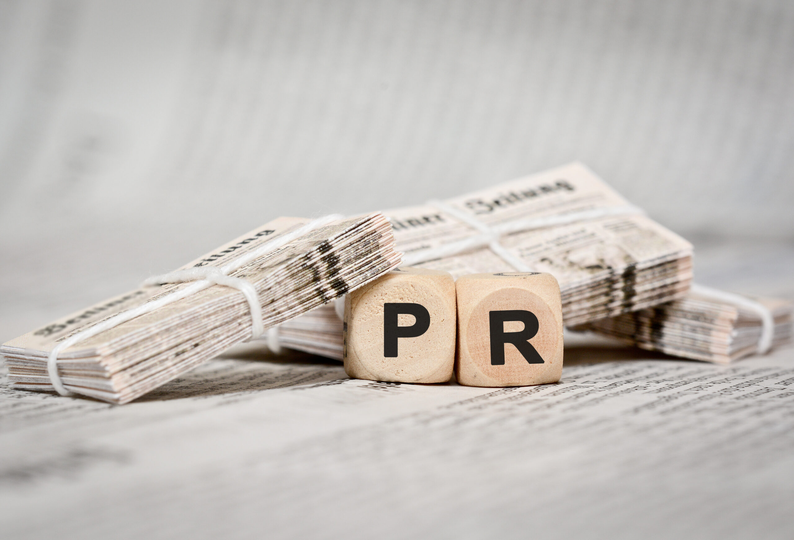 Stacks of folded newspapers bound with string, with wooden blocks spelling PR in the foreground.