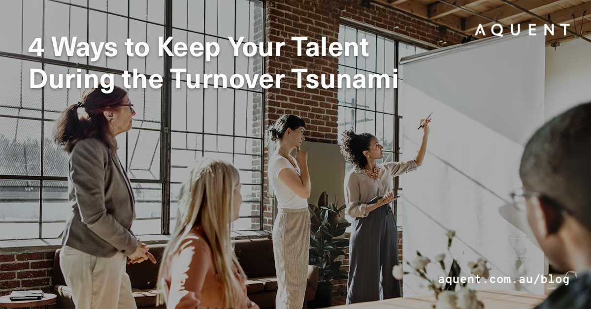 Group of professionals in a brick-walled studio watching a presenter point to a whiteboard; banner reads '4 Ways to Keep Your Talent During the Turnover Tsunami' with the Aquent logo.