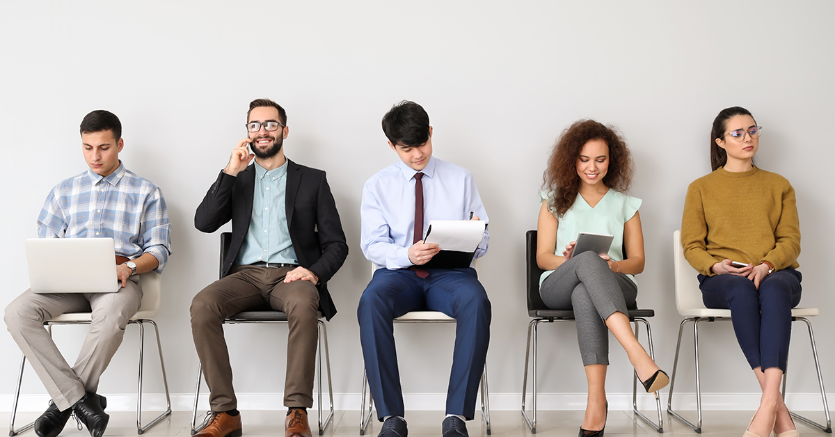Five diverse people sit in a row in a modern waiting area, each using a device or document (laptop, phone, papers, tablet).