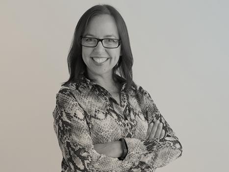Smiling woman with glasses and a snakeskin-patterned shirt standing with arms crossed against a neutral background.