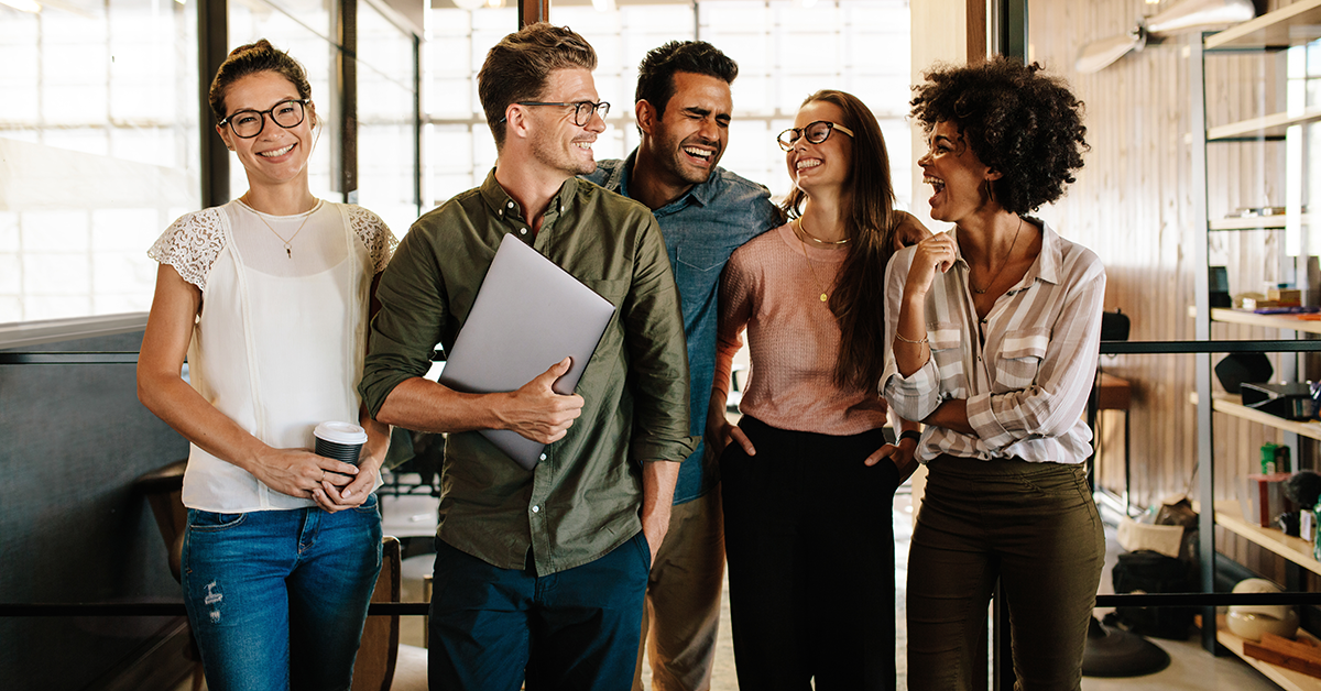 Group of five coworkers in a bright open-office, laughing and chatting together.