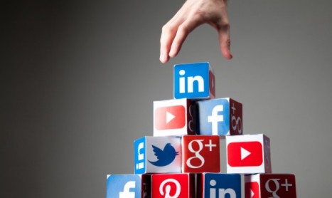 A hand placing a LinkedIn logo cube on top of a pyramid made of social media icons, representing networking.