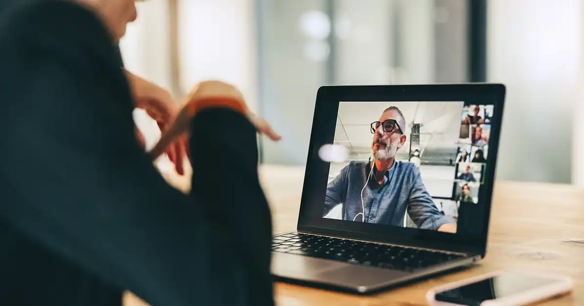 Businesswoman speaking during a virtual team meeting on her laptop. Her team is visible on the laptop screen.