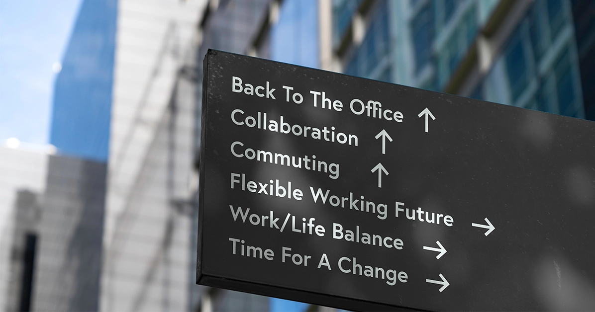 Black outdoor sign listing workplace goals: 'Back To The Office', 'Collaboration', 'Commuting' with up arrows, and 'Flexible Working Future', 'Work/Life Balance', 'Time For A Change' with right arrows.