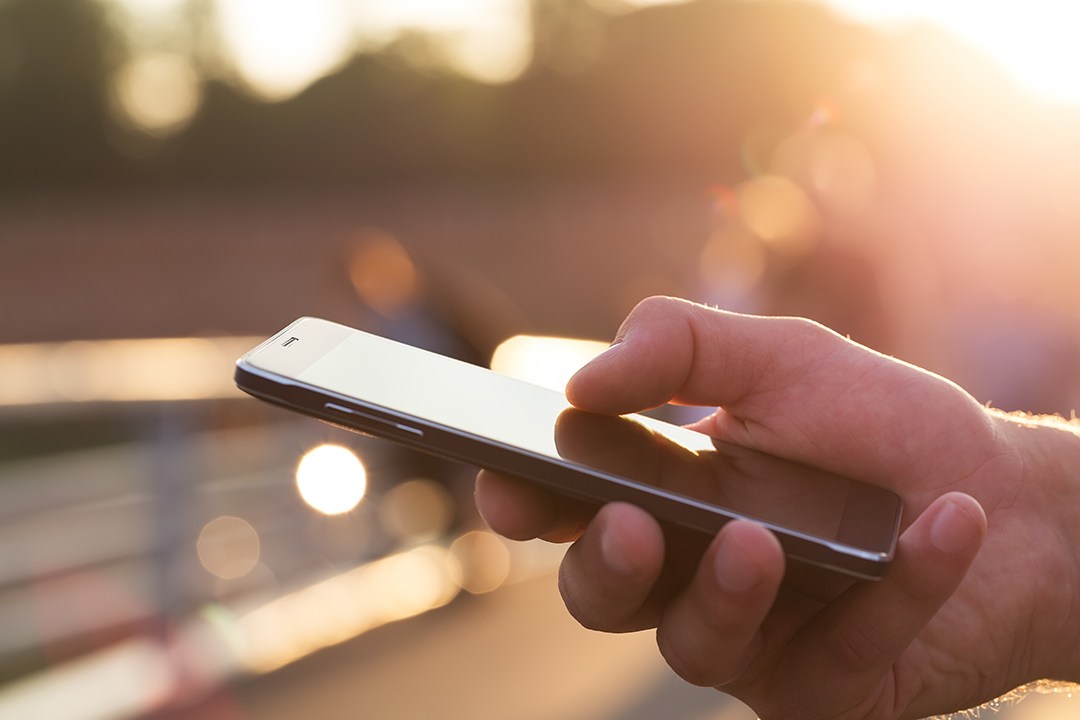 Close-up of a hand holding a smartphone outdoors during sunset with warm golden light.