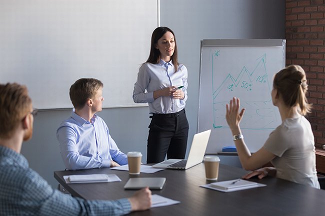 Person stood next to whiteboard facing three people sat at a table