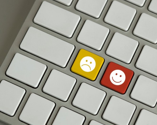 Close-up of two emoji keys on a keyboard: yellow frowning face and red smiling face among white keys, for user feedback.