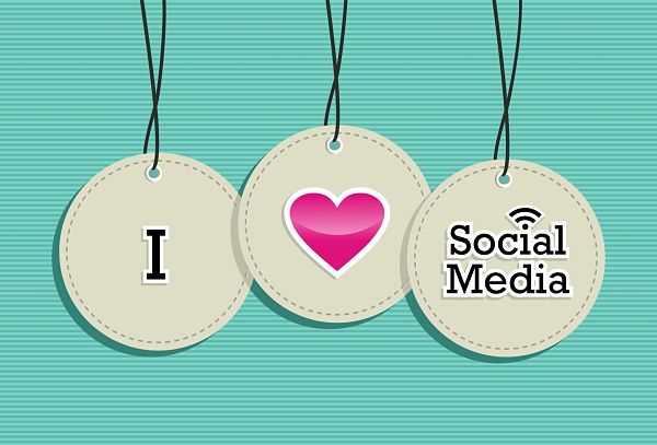 Three hanging circular tags spell out 'I love Social Media' with a pink heart in the middle on a teal striped background.