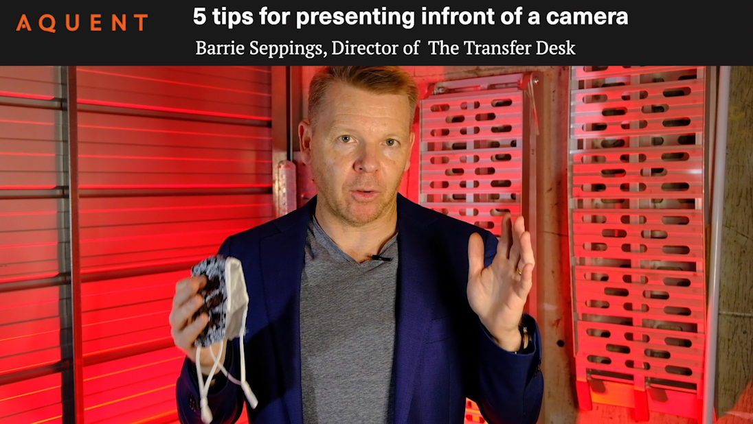 Man in a navy blazer explains five camera tips in a red-lit studio, holding a face mask in one hand.