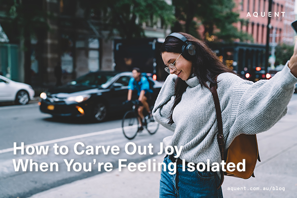 Woman with headphones on a city sidewalk, arms outstretched in joy; a blog image about carving out joy when feeling isolated