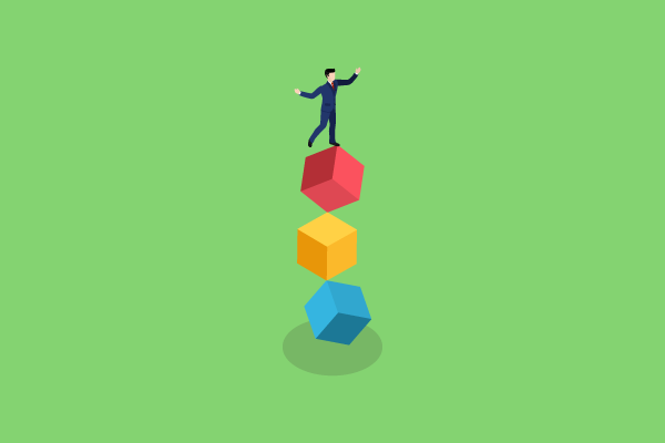 Person in a blue suit balancing on the top red cube of a stack (red, yellow, blue) on a bright green background, with a shadow below.